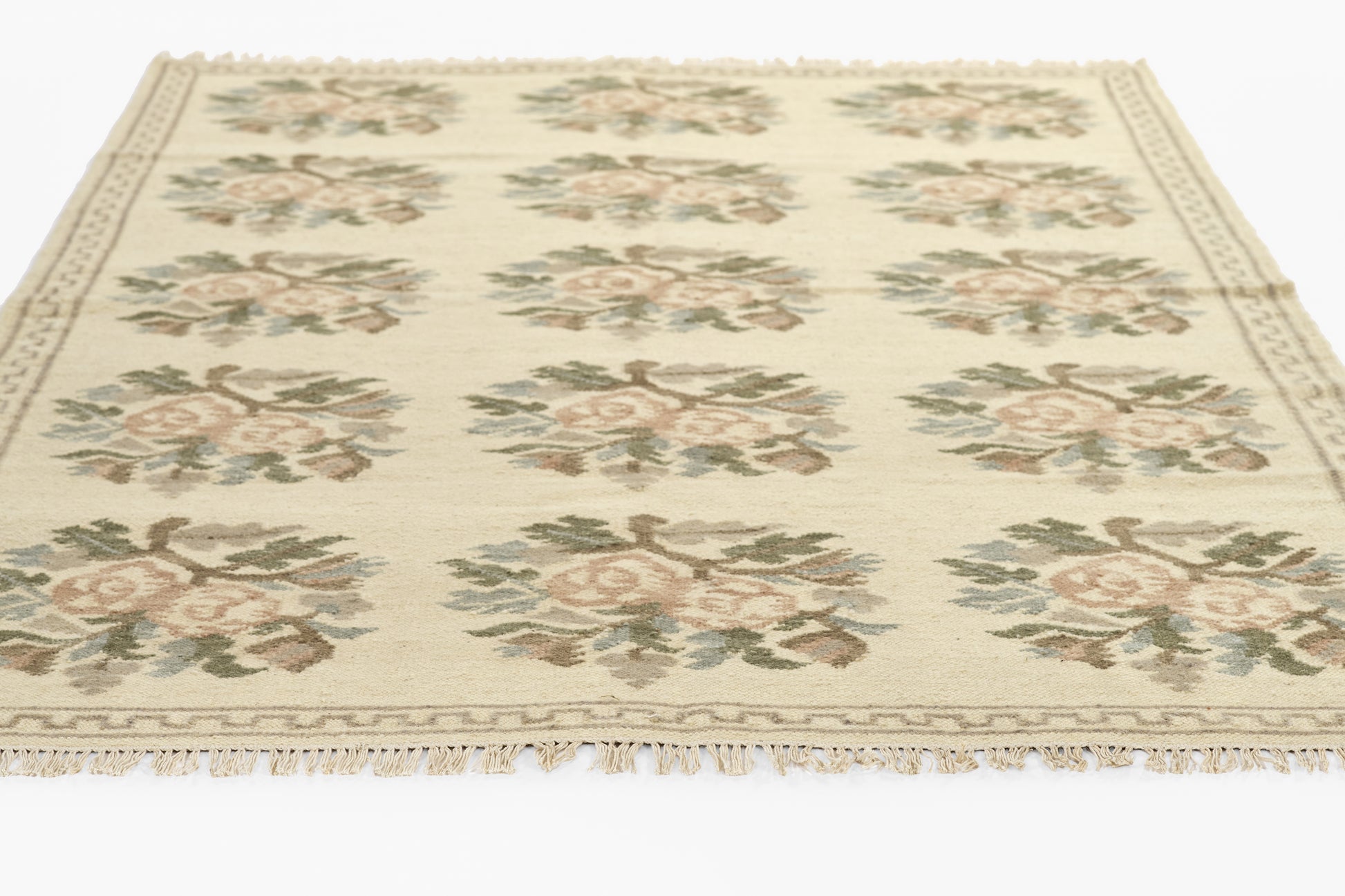 Cream rug with repeating pink rose bouquets and green leaves, tasseled fringe along edges.