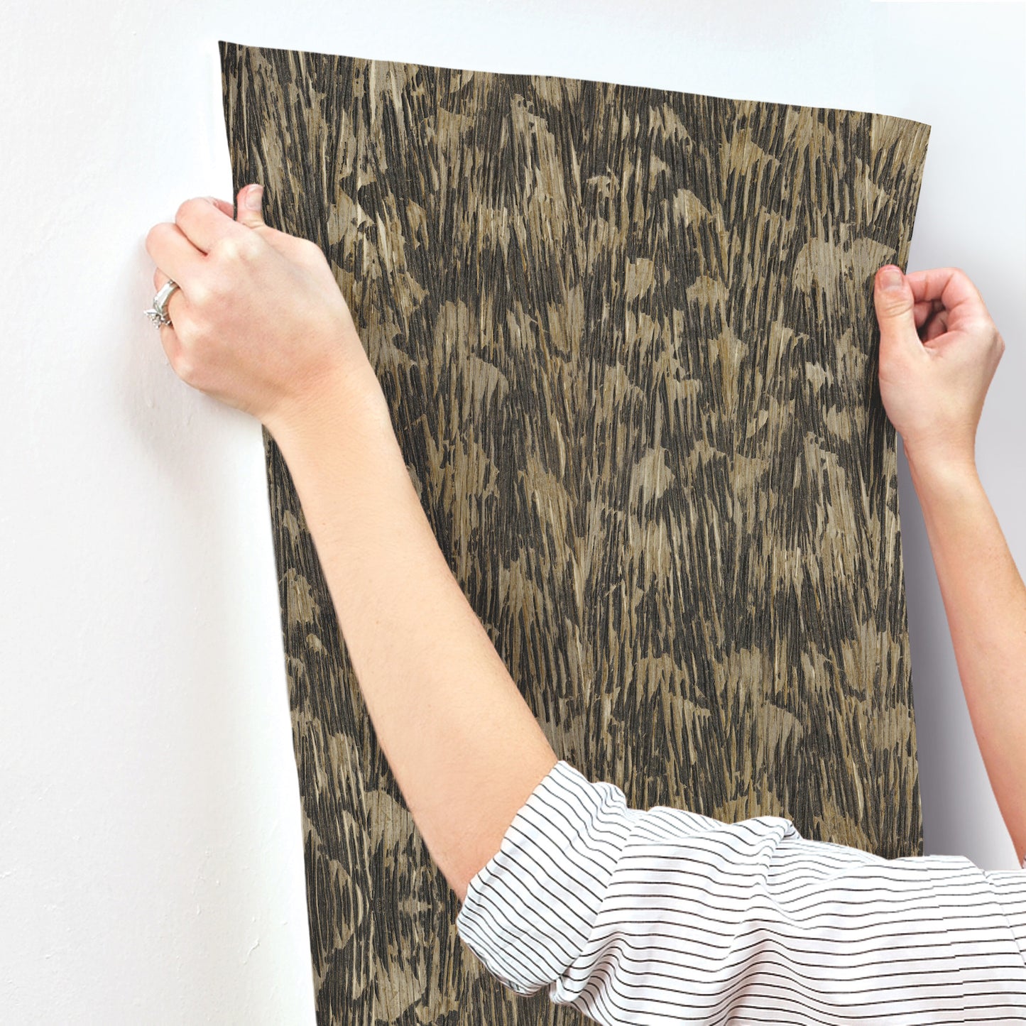 Black wallpaper with gilded plume pattern, held by two hands.