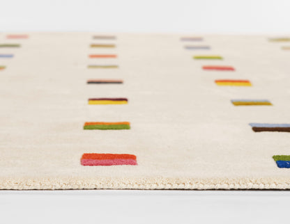 Beige woven area rug with small rectangular blocks in red, blue, green and orange; modern geometric design.