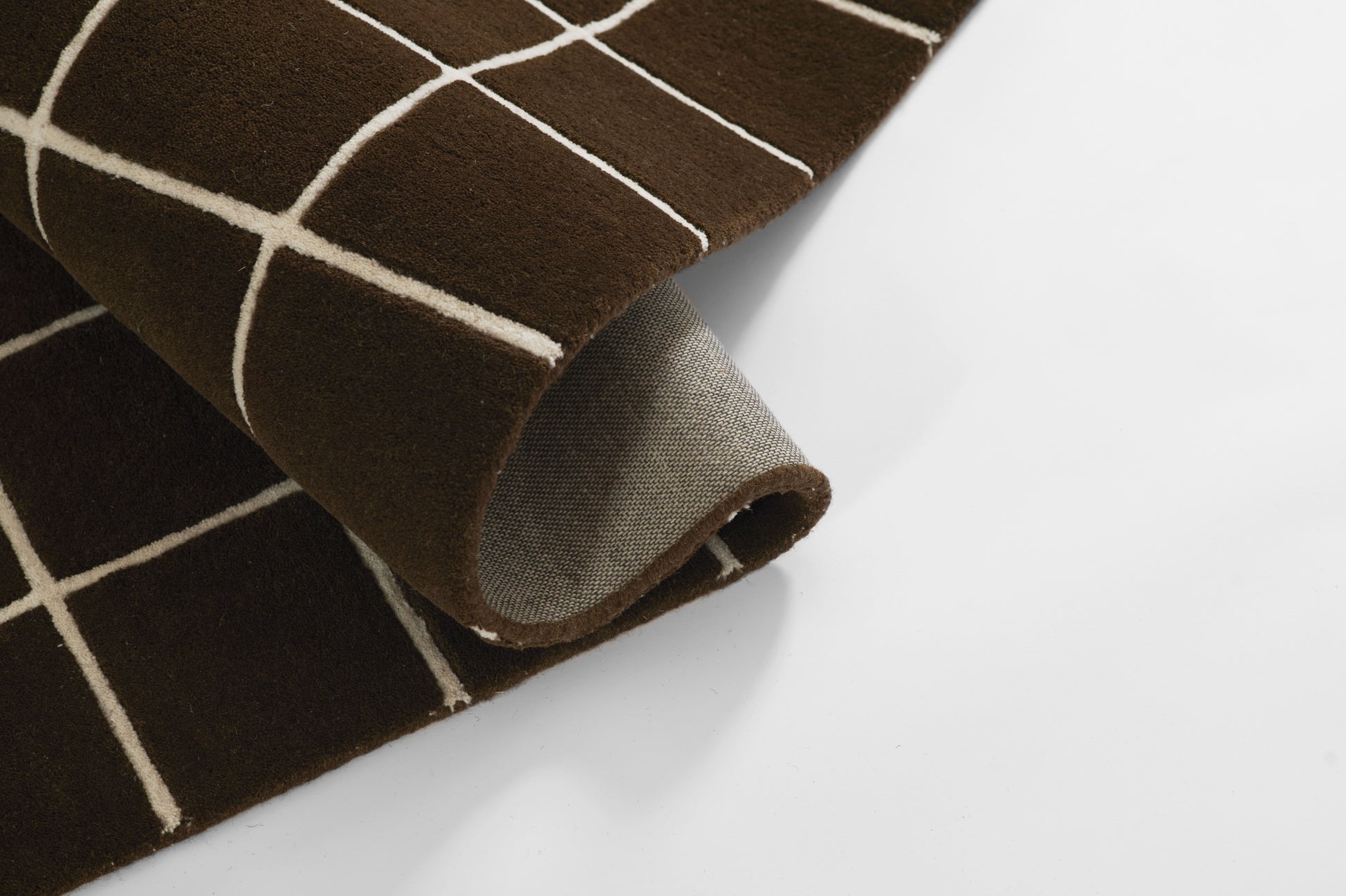 Brown grid-pattern rug, partially rolled to reveal grey underside, cozy floor decor.