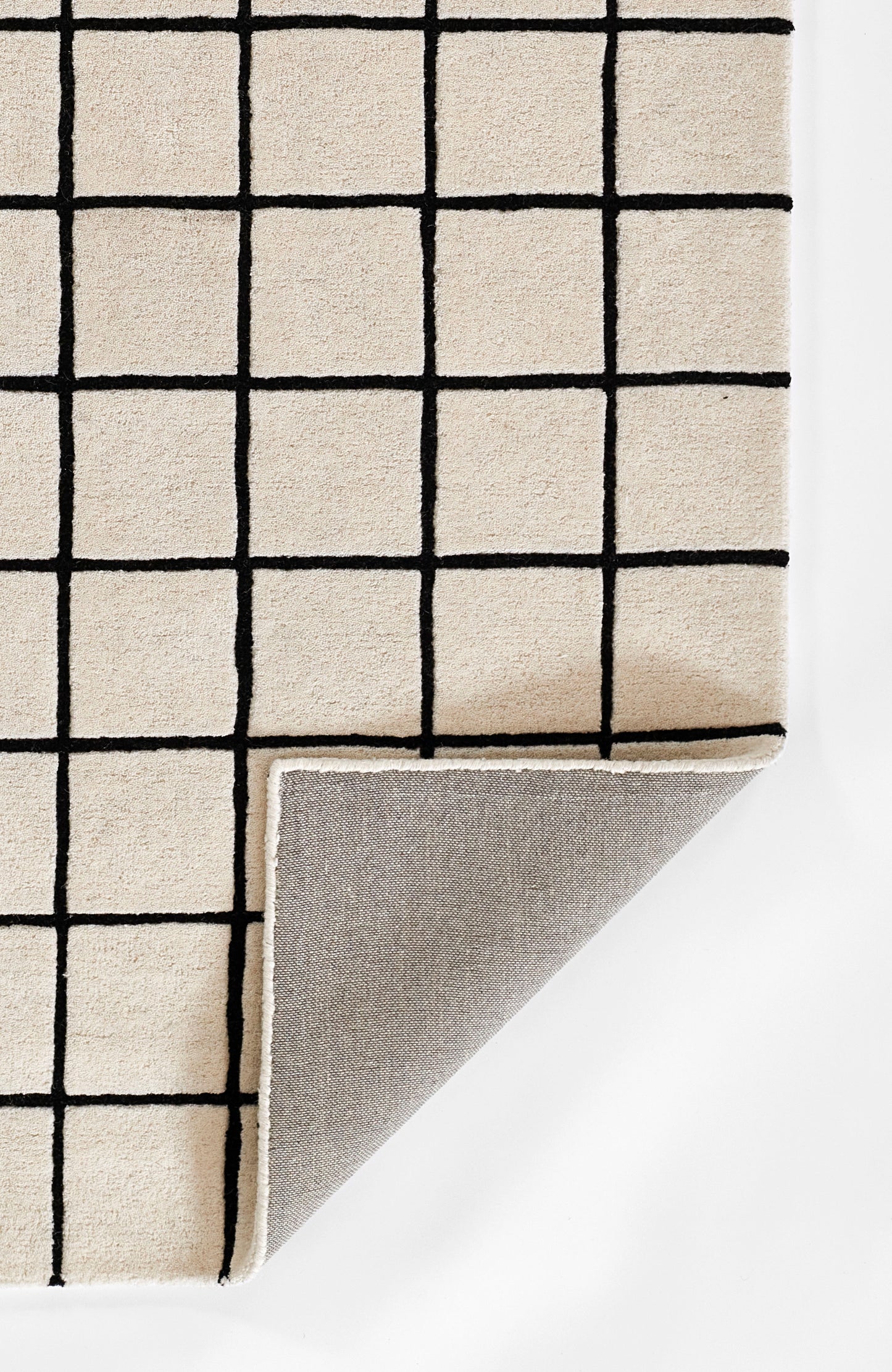 Beige grid-pattern rug with bold black lines; folded corner reveals gray underside.