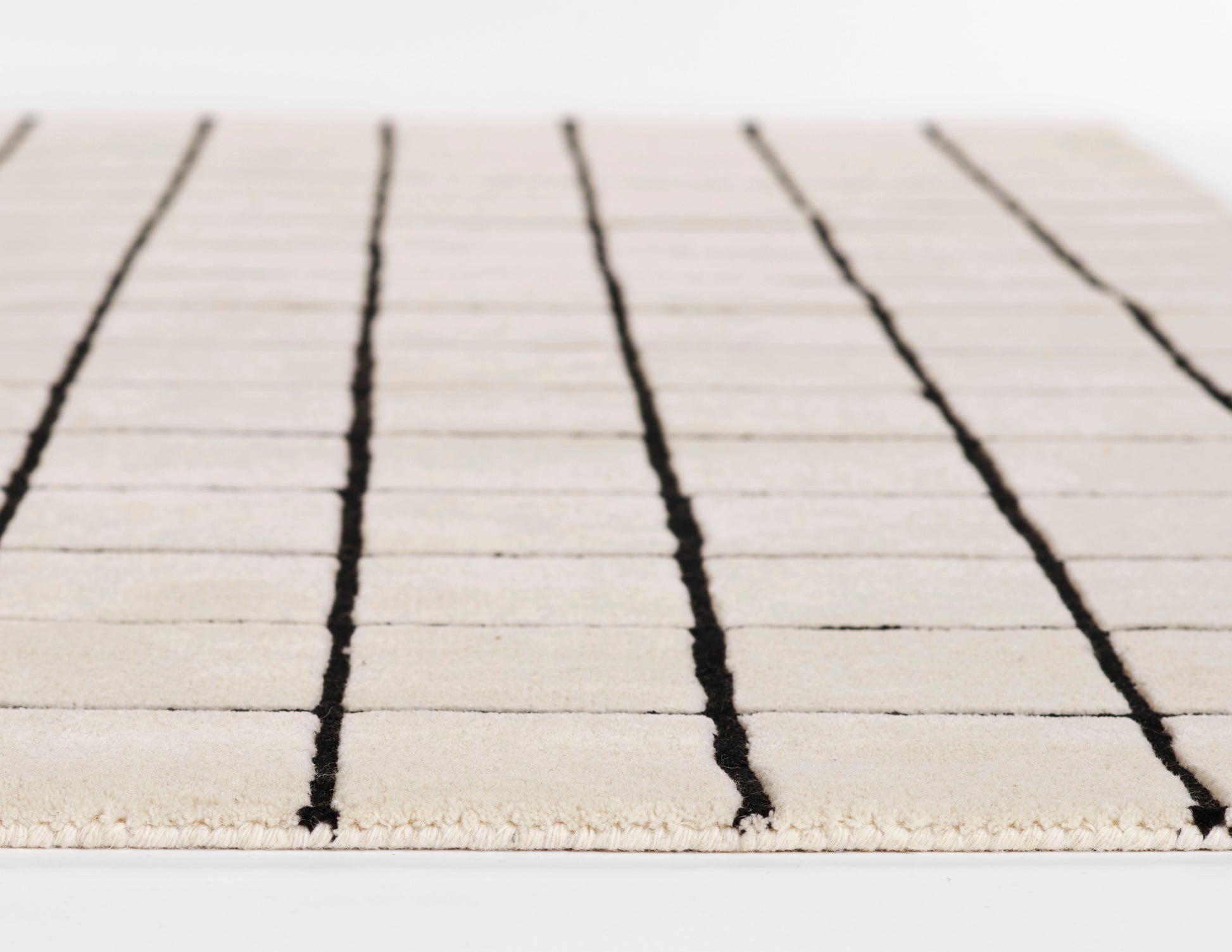 Beige flatwoven rug with bold black vertical stripes and a fringed edge for a modern minimalist look.