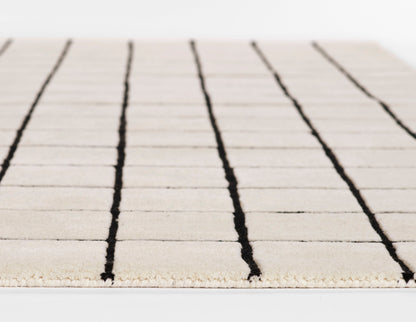 Beige rug with bold black vertical stripes and a fringed edge, minimalist modern design.
