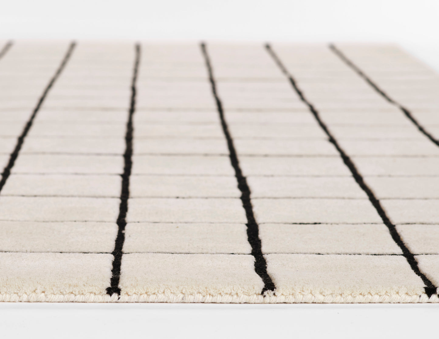 Ivory rug with black vertical stripes, woven texture and fringe edge; modern minimalist design.