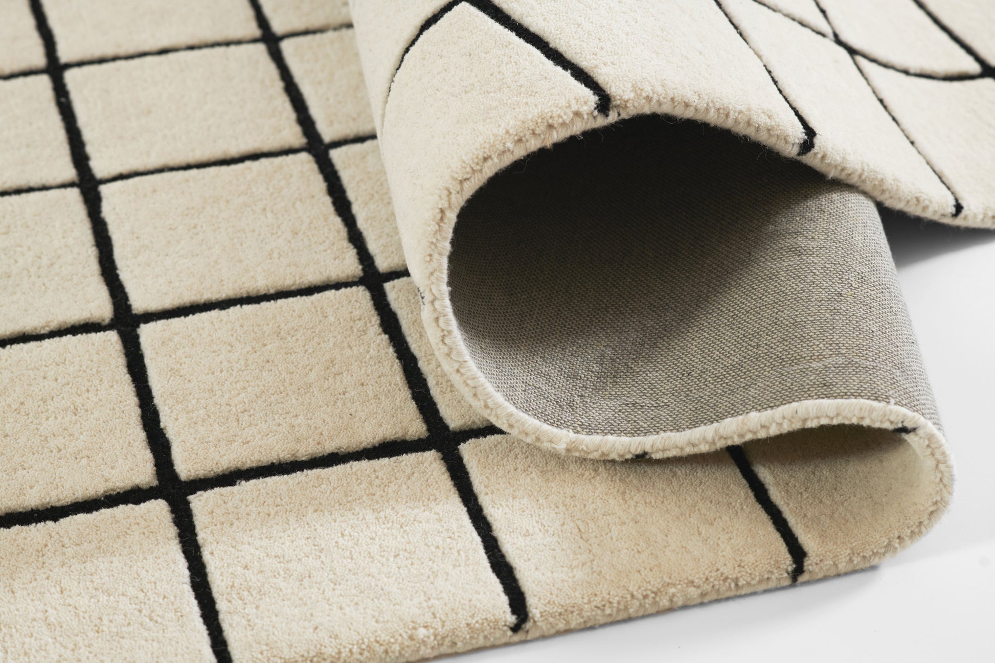 Beige plush runner with bold black grid lines, folded corner reveals soft underside.