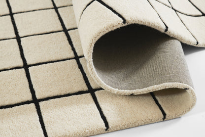 Beige rug with black grid pattern, folded corner showing soft pile and light grey underside.