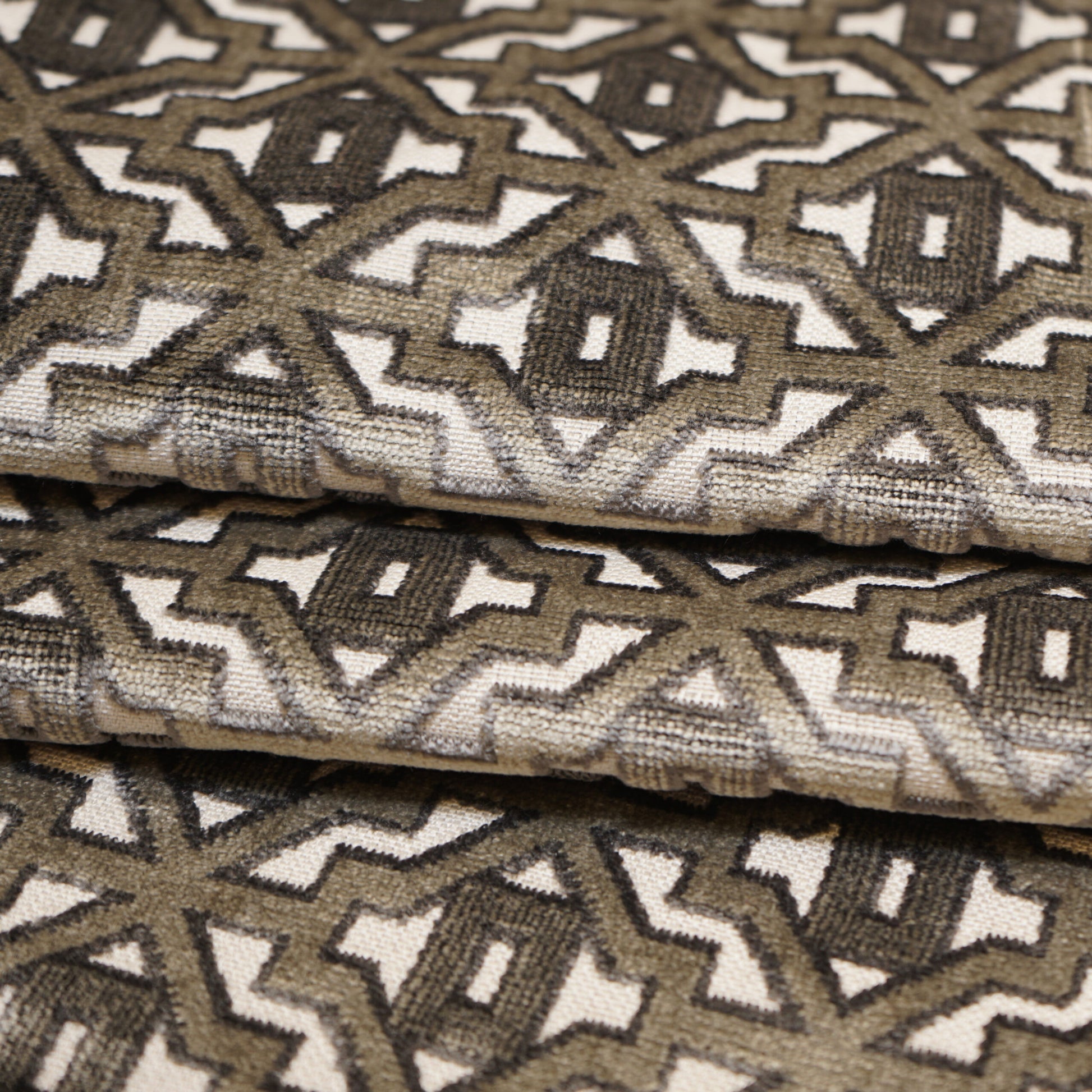 Velvet fabric with interlocking diamond geometric pattern in grey & silver on cream background; folded.