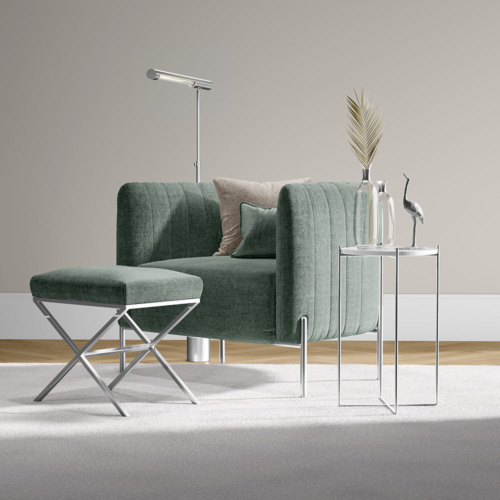 Green spearmint solid fabric armchair with matching ottoman, chrome legs, beside a glass-top side table with vase, palm leaf, bird sculpture and floor lamp.