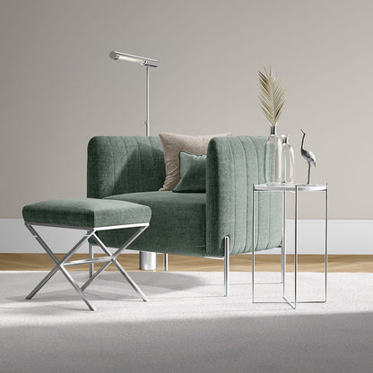 Green spearmint solid fabric armchair with matching ottoman, chrome legs, beside a glass-top side table with vase, palm leaf, bird sculpture and floor lamp.