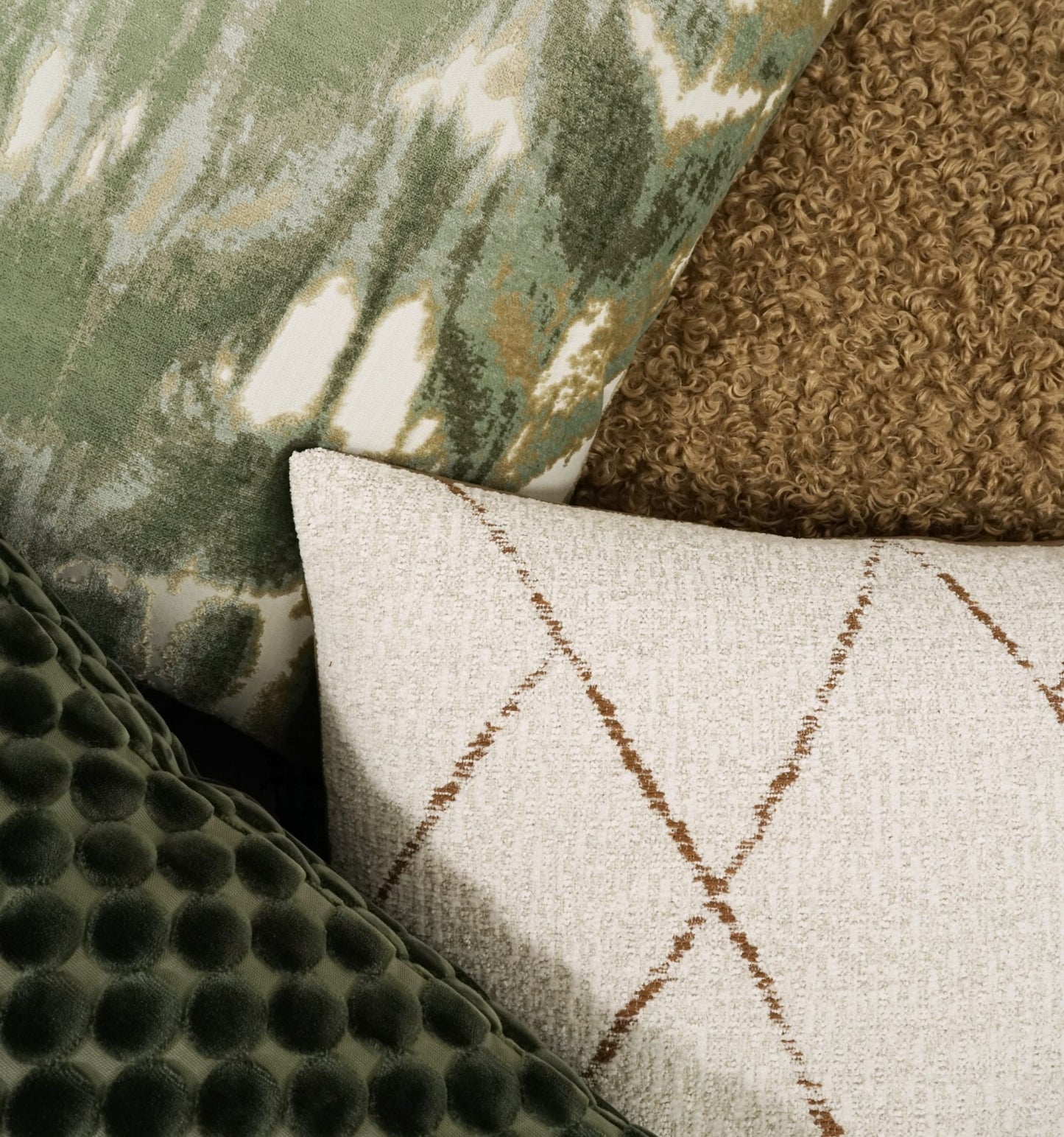 Pile of decorative cushions in green tones: velvet with circles, olive patterned fabric, beige lattice, and brown boucle.
