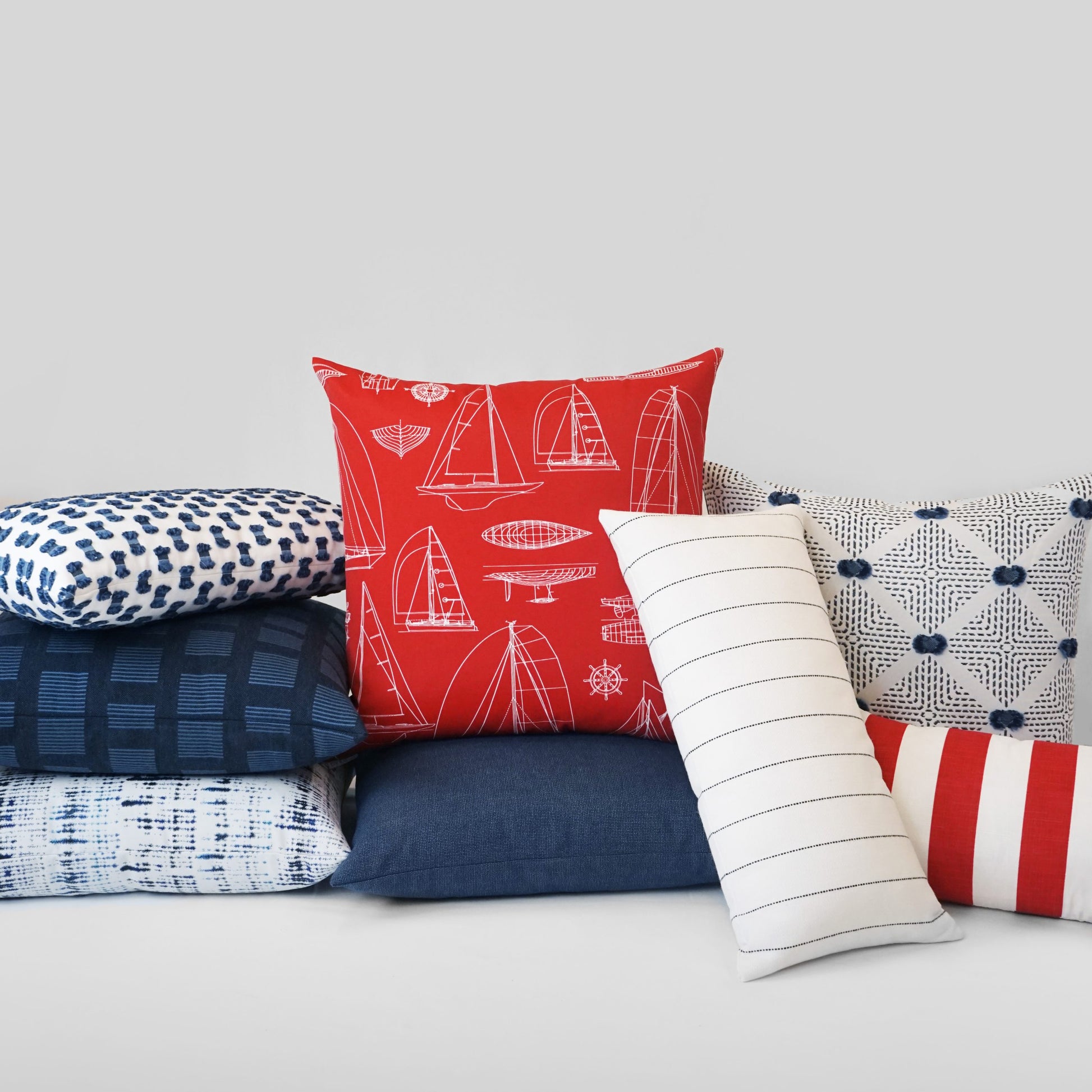 Nautical outdoor lumbar pillow in red, navy and white with sailboat print, stripes and geometric patterns.