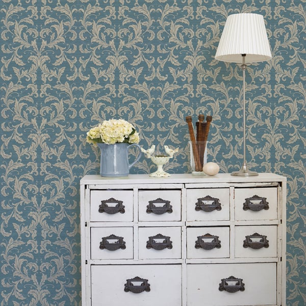 Vintage white dresser with 12 drawers, dark handles; blue damask wallpaper; lamp and blue pitcher with flowers.