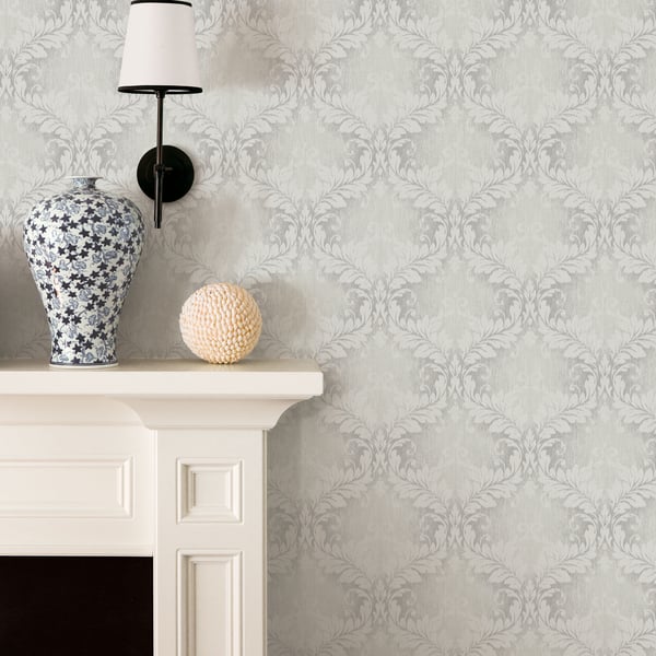 Blue and white floral ceramic vase on a white mantel, beige orb, and a black wall lamp against grey damask wallpaper.