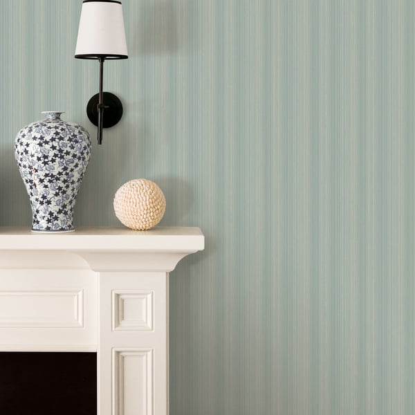Blue-and-white floral ceramic vase and beige textured decorative ball on a white mantel with a black wall lamp against mint striped wallpaper.
