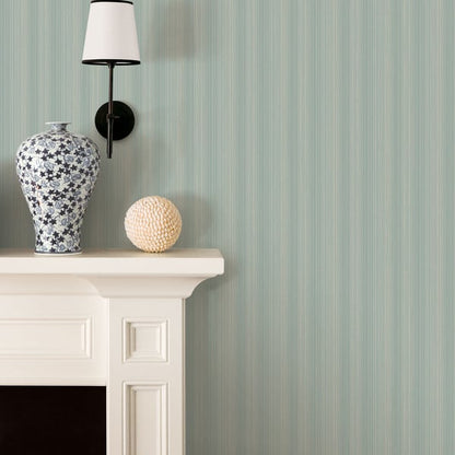 Blue-and-white floral ceramic vase and beige textured decorative ball on a white mantel with a black wall lamp against mint striped wallpaper.