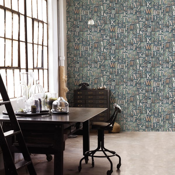 Industrial vintage home office: dark wood desk, rolling chair, glass domes, and green letter-pattern wallpaper.