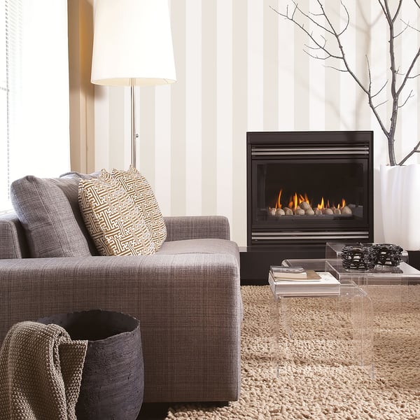 Modern living room with gray sofa, patterned pillow, glass coffee table, gas fireplace, striped wallpaper, shag rug.