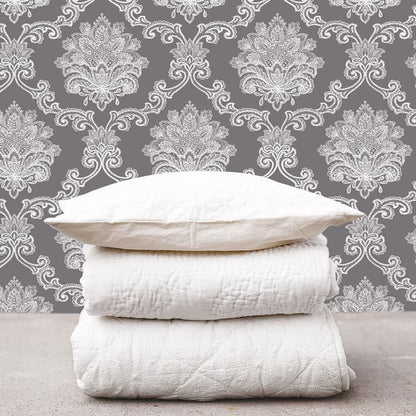 Stack of white pillows, a quilt, and a blanket against black damask wallpaper.