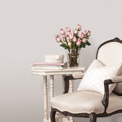 Vintage cream chair with dark wood trim beside a distressed white table, glass vase of pink roses, a round white box and books.