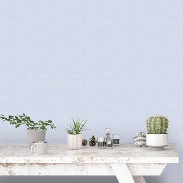 Blue plain linen wallpaper on the wall behind a rustic white table with potted plants, glass jars, a mug, and a cactus in a white pot.