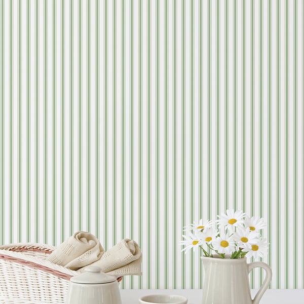 Beige baby booties on a wicker basket beside a white mug with daisies against green striped wallpaper.