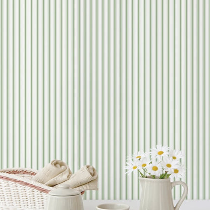 Beige baby booties on a wicker basket beside a white mug with daisies against green striped wallpaper.