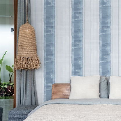 Boho bedroom with blue striped wallpaper, woven rattan pendant lamp, gray curtains, neutral bedding and wooden headboard.