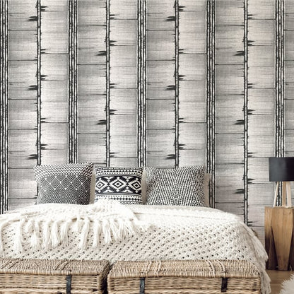 Neutral boho bedroom with a low woven rattan bed, cream knit throw, geometric cushions, silver grey striped wallpaper, wooden lamp table