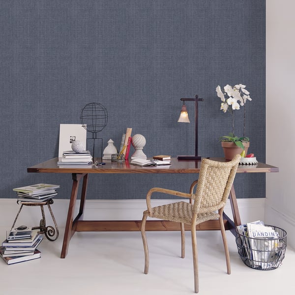 Mid-century desk with angled legs, beige woven chair, blue textured wall; books, lamp, globe, and white orchid.