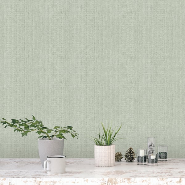 Sage green textured wall behind a whitewashed table with a gray pot plant, ribbed pink planter, mug, pinecones & glass jars.