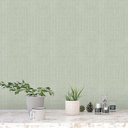 Sage green textured wall behind a whitewashed table with a gray pot plant, ribbed pink planter, mug, pinecones & glass jars.