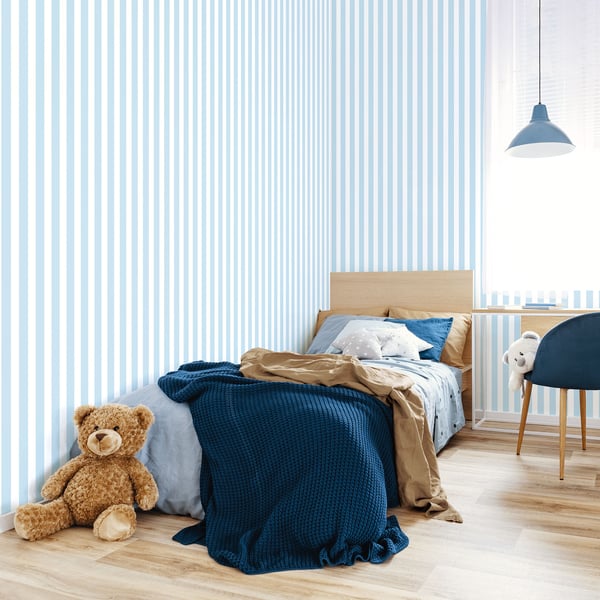 Kids bedroom with blue striped wallpaper, wooden single bed, navy throw, teddy bear, blue chair, pendant lamp