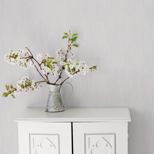 Floral wallpaper featuring white blossoms and green leaves on a soft silver-grey background with a wispy texture.