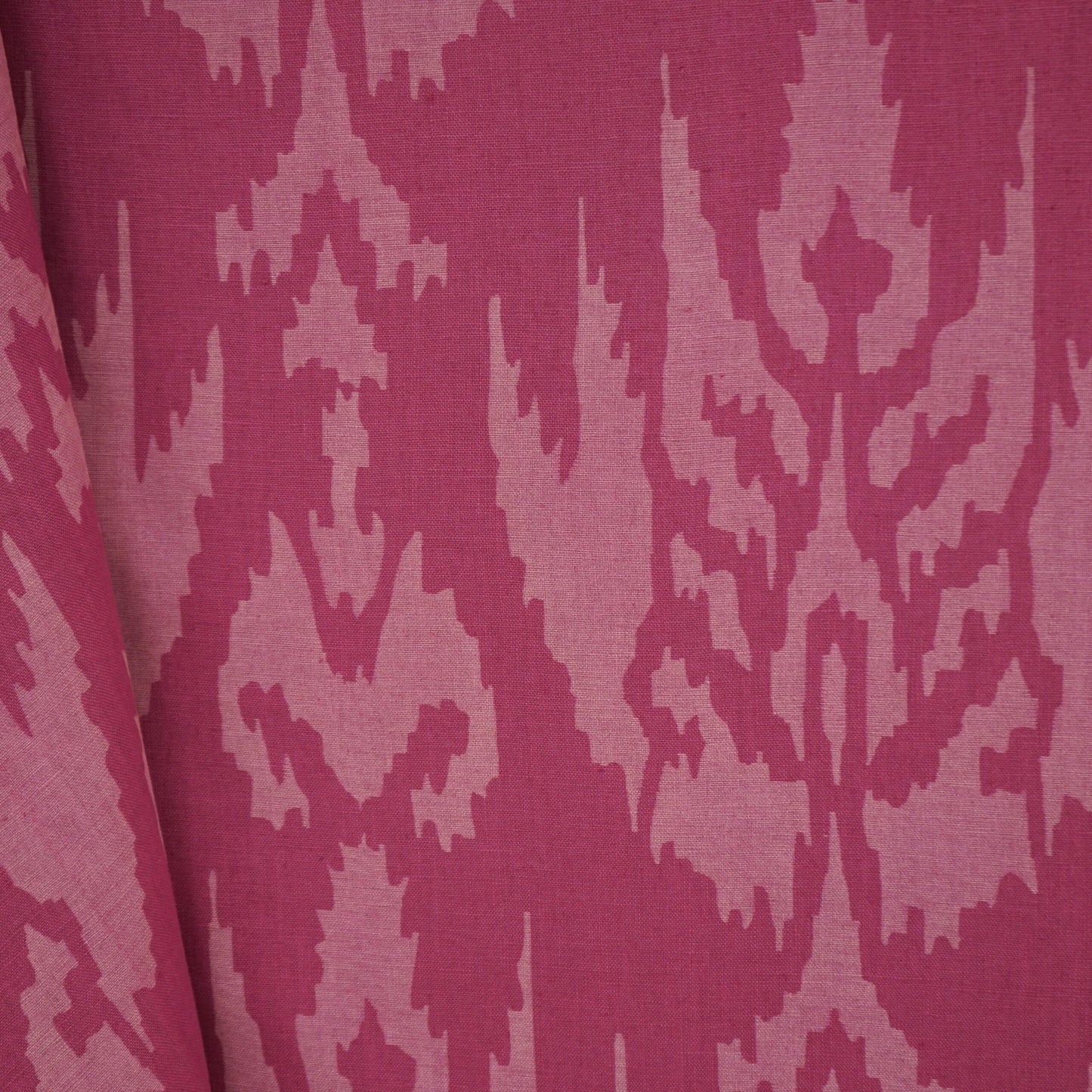 Magenta jacquard fabric with light pink damask/ikat motif and a folded edge.