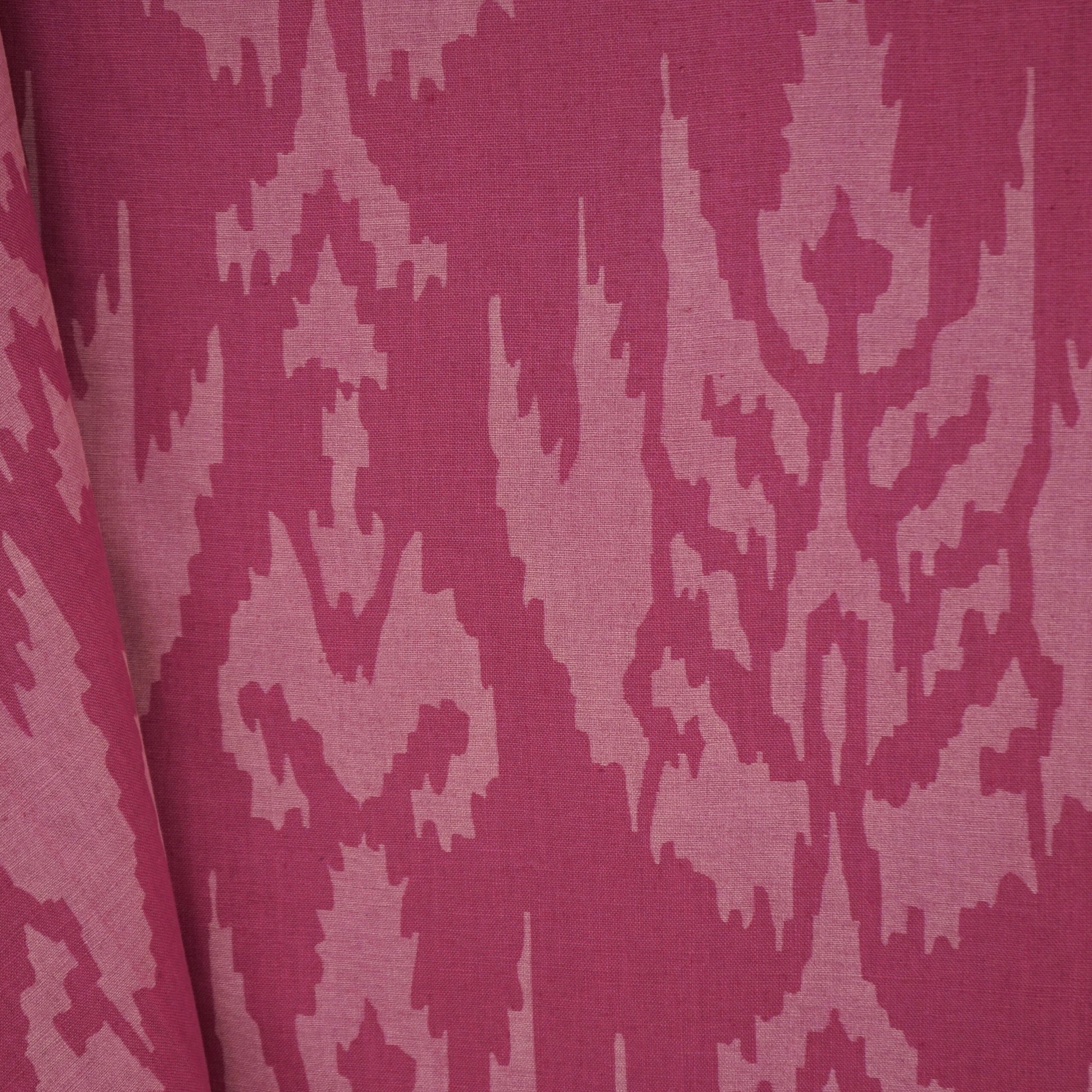 Magenta jacquard fabric with light pink damask/ikat motif and a folded edge.