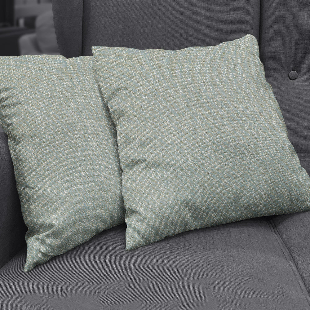 Pair of teal-green textured throw pillows with white speck pattern on a dark gray fabric sofa.