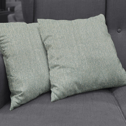 Pair of teal-green textured throw pillows with white speck pattern on a dark gray fabric sofa.