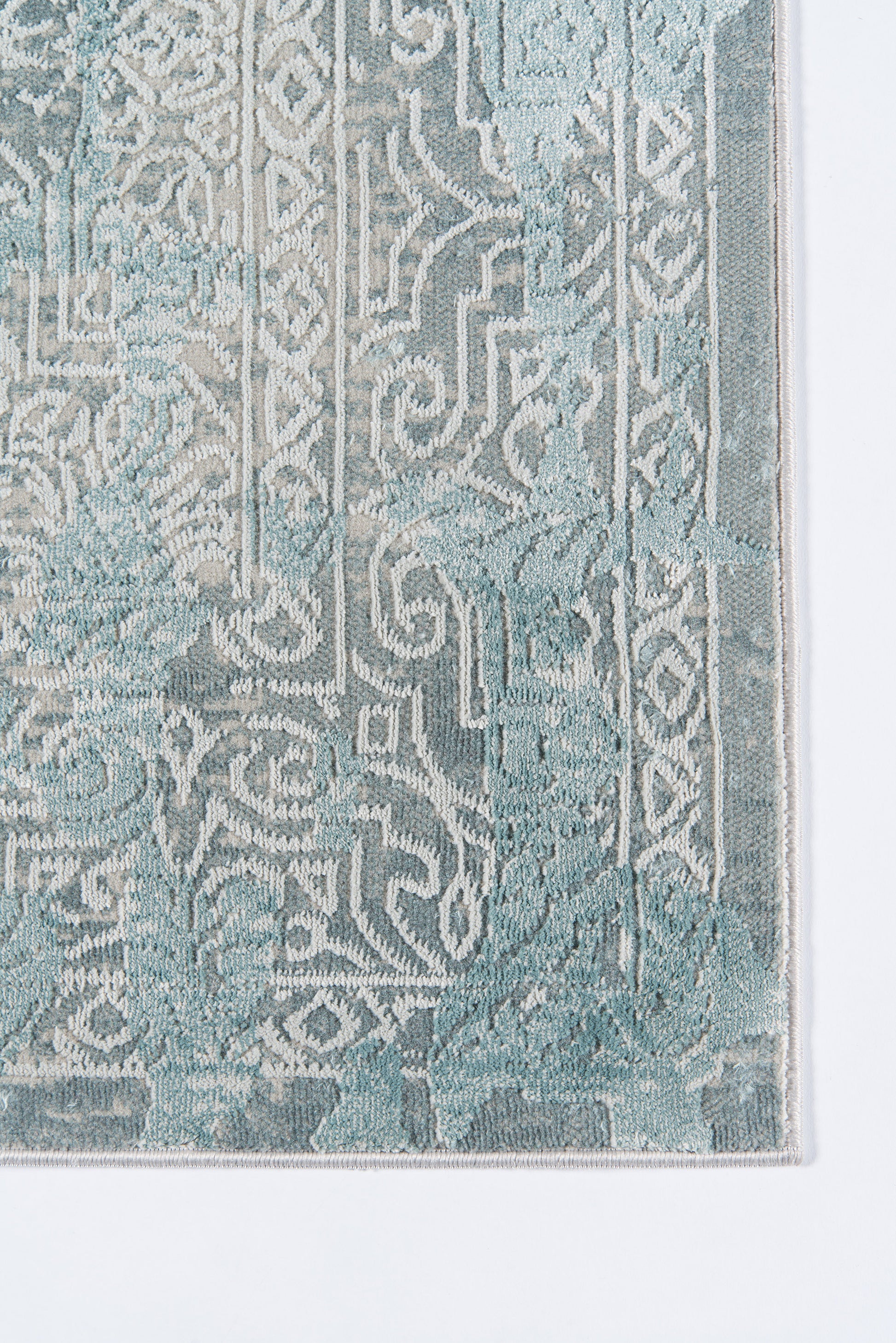 Teal rug with white ornate arabesque pattern and geometric border, close-up edge.