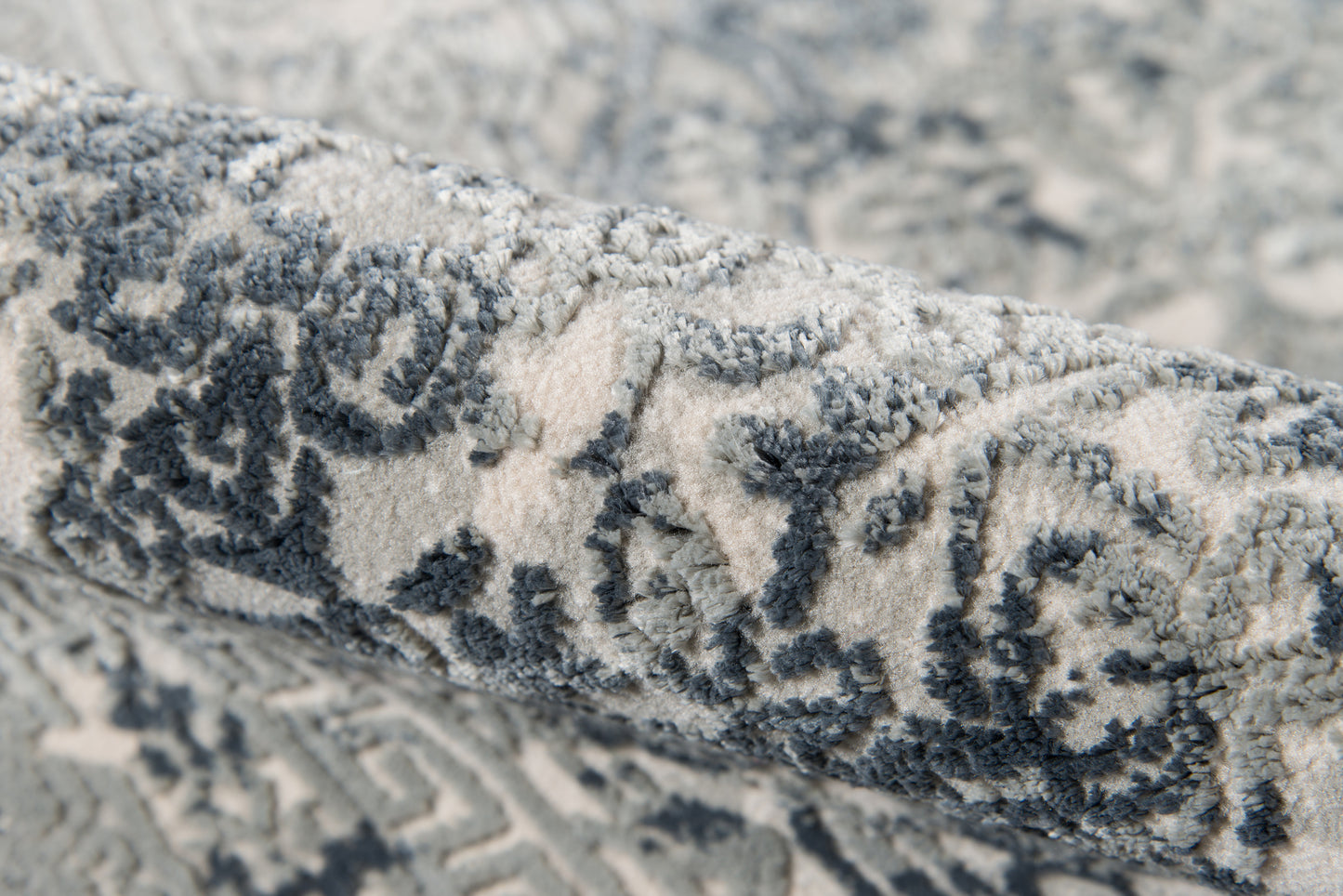 Rolled gray-blue patterned rug with an ornate motif and a plush woven pile.