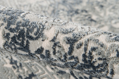 Rolled gray-blue patterned rug with an ornate motif and a plush woven pile.