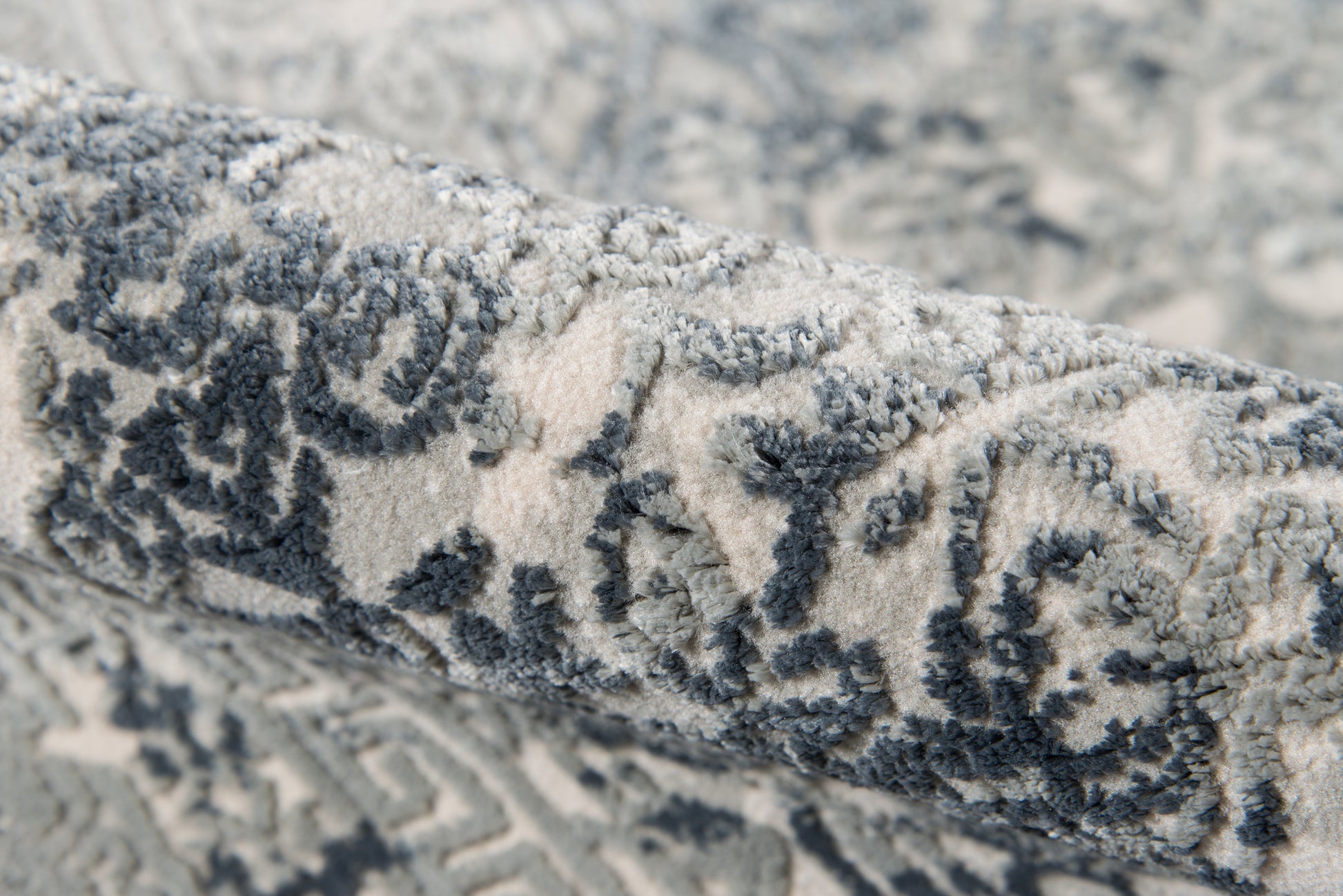 Rolled blue-gray and ivory Persian-style rug with intricate floral damask pattern and woven texture.