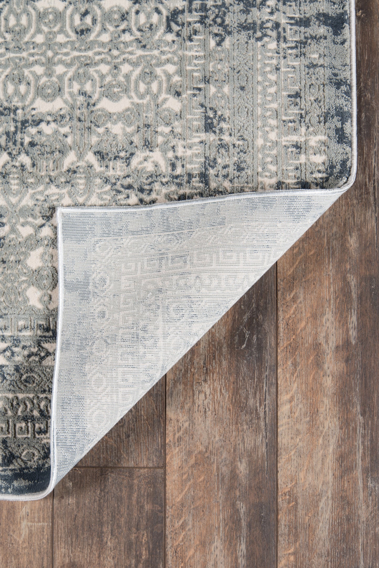 Navy & light gray distressed patterned area rug on dark wood floor; folded corner shows pale gray underside.
