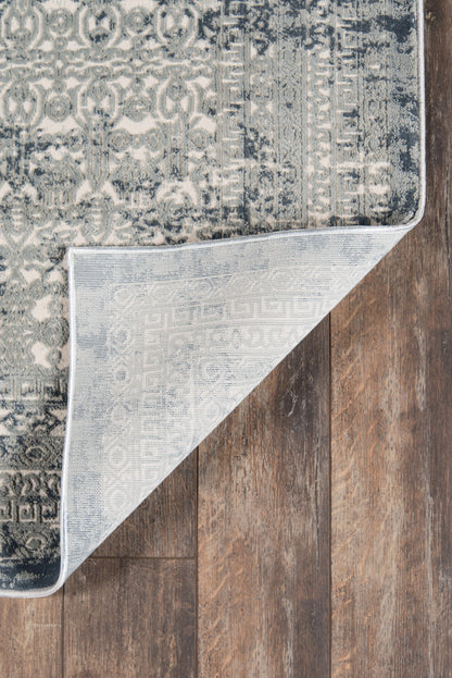 Blue-gray distressed patterned area rug with medallion motifs; folded corner reveals pale underside on dark wood floor.