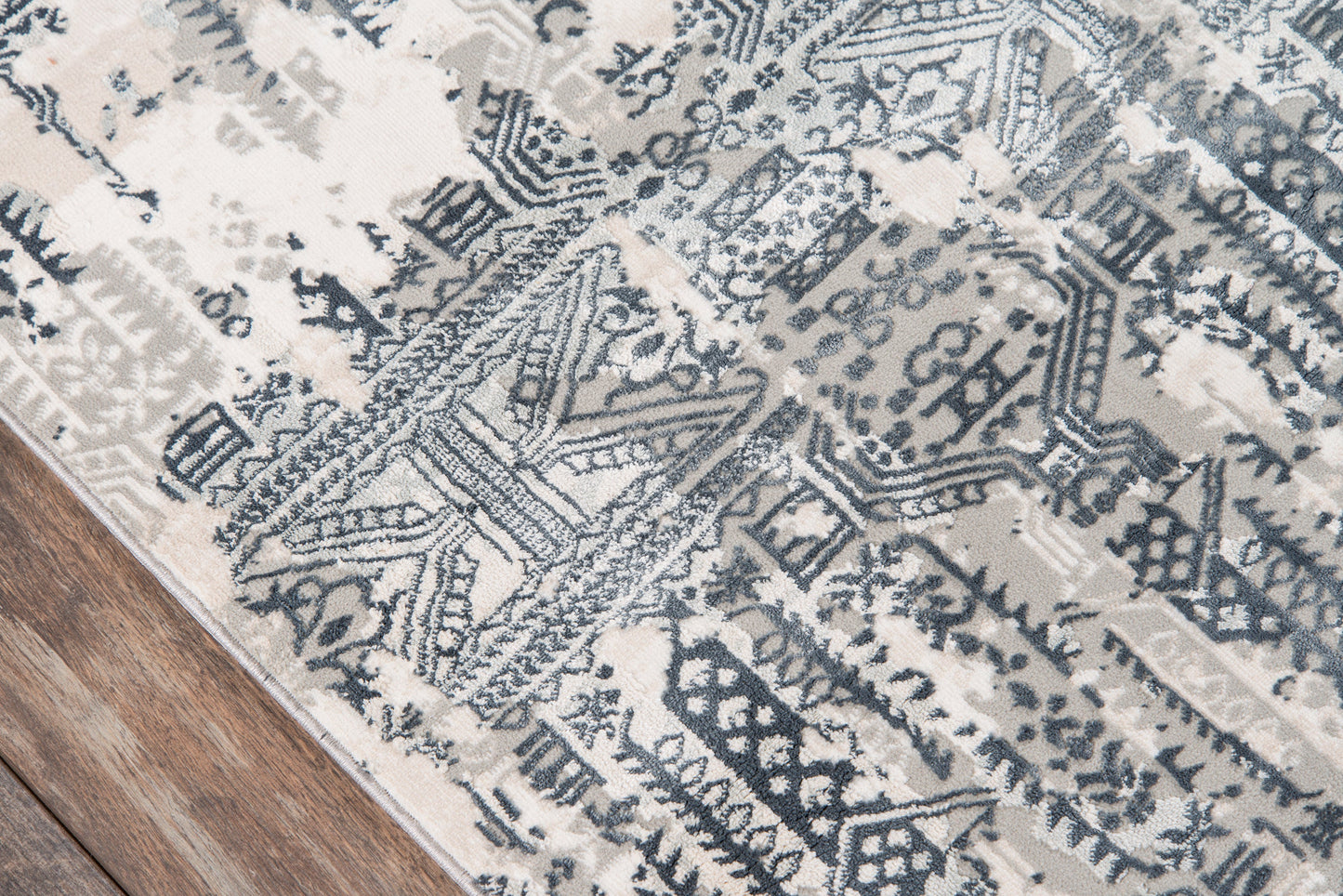 Gray-blue geometric tribal rug with ivory accents on a wooden floor.