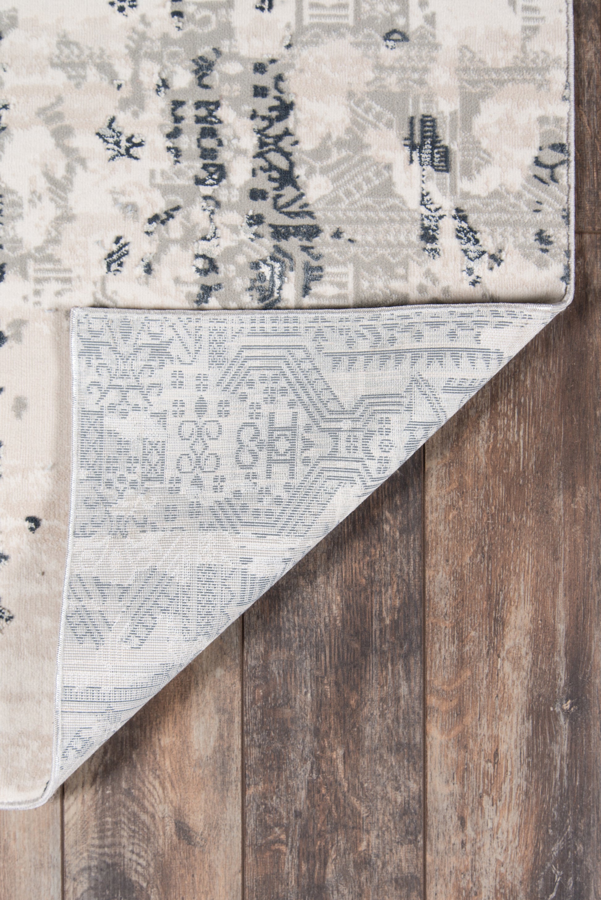 Gray and ivory patterned rug with floral/geometric motifs, folded corner reveals pale blue underside on a wood floor.