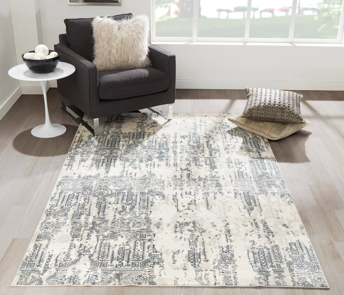 Rectangular gray and ivory distressed abstract area rug in a modern living room with a dark armchair and fluffy pillow.