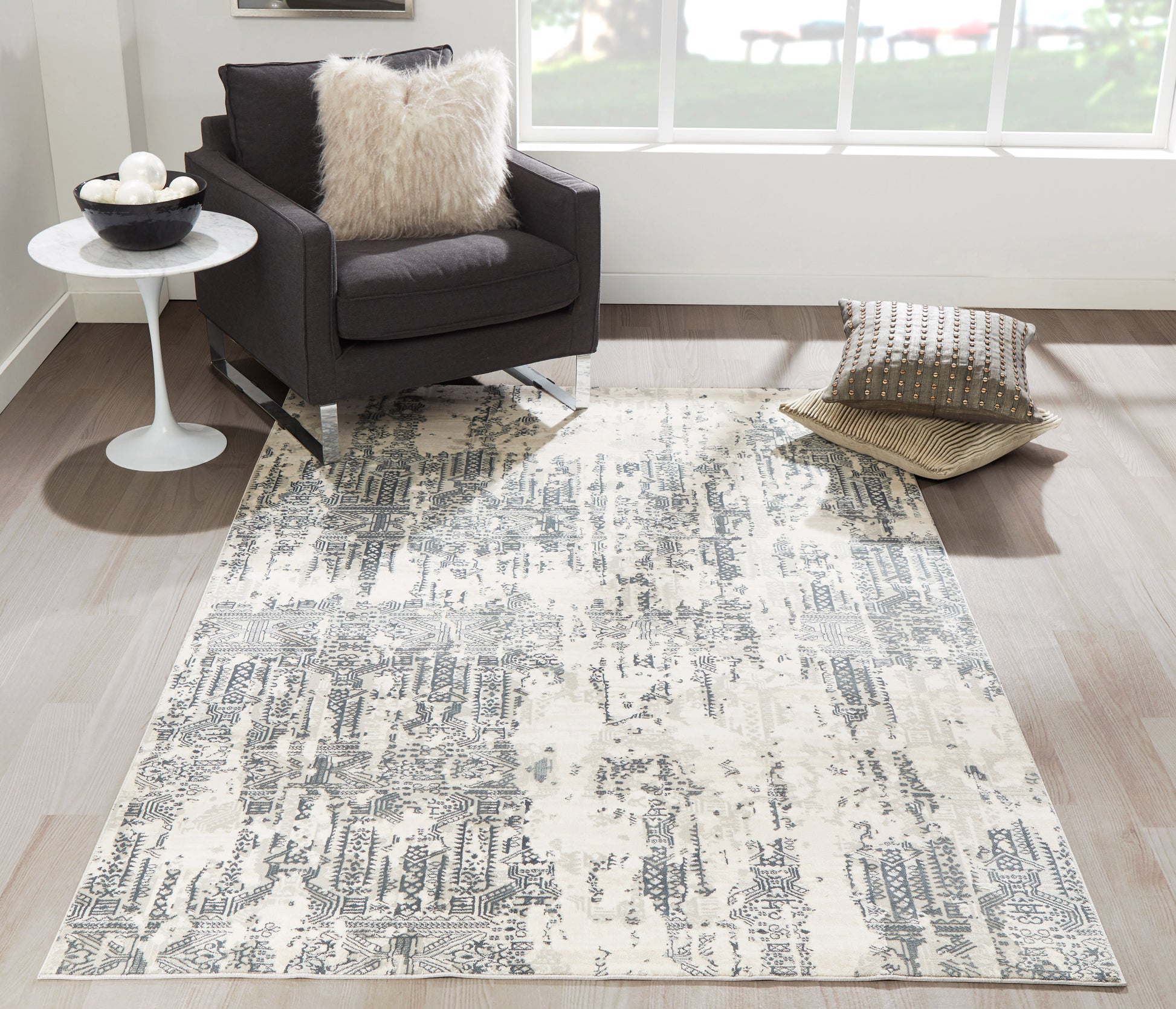 Rectangular gray and ivory distressed abstract area rug in a modern living room with a dark armchair and fluffy pillow.