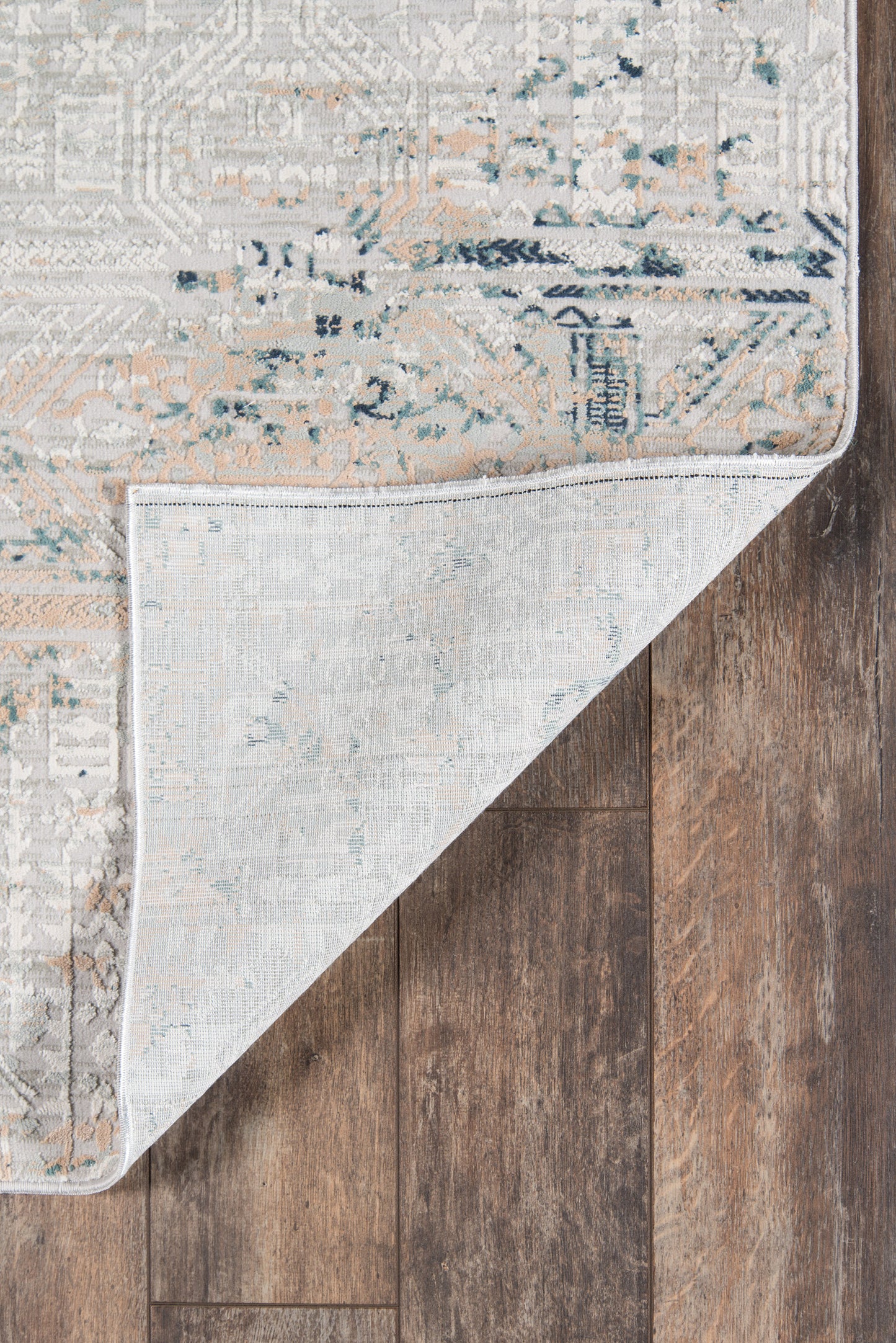 Rectangular vintage rug in muted gray-beige with blue and peach accents; folded corner shows light underside on dark wood.