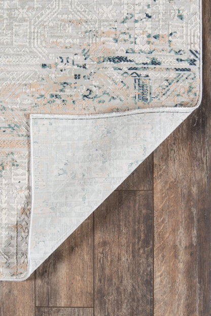 Rectangular vintage rug in muted gray-beige with blue and peach accents; folded corner shows light underside on dark wood.