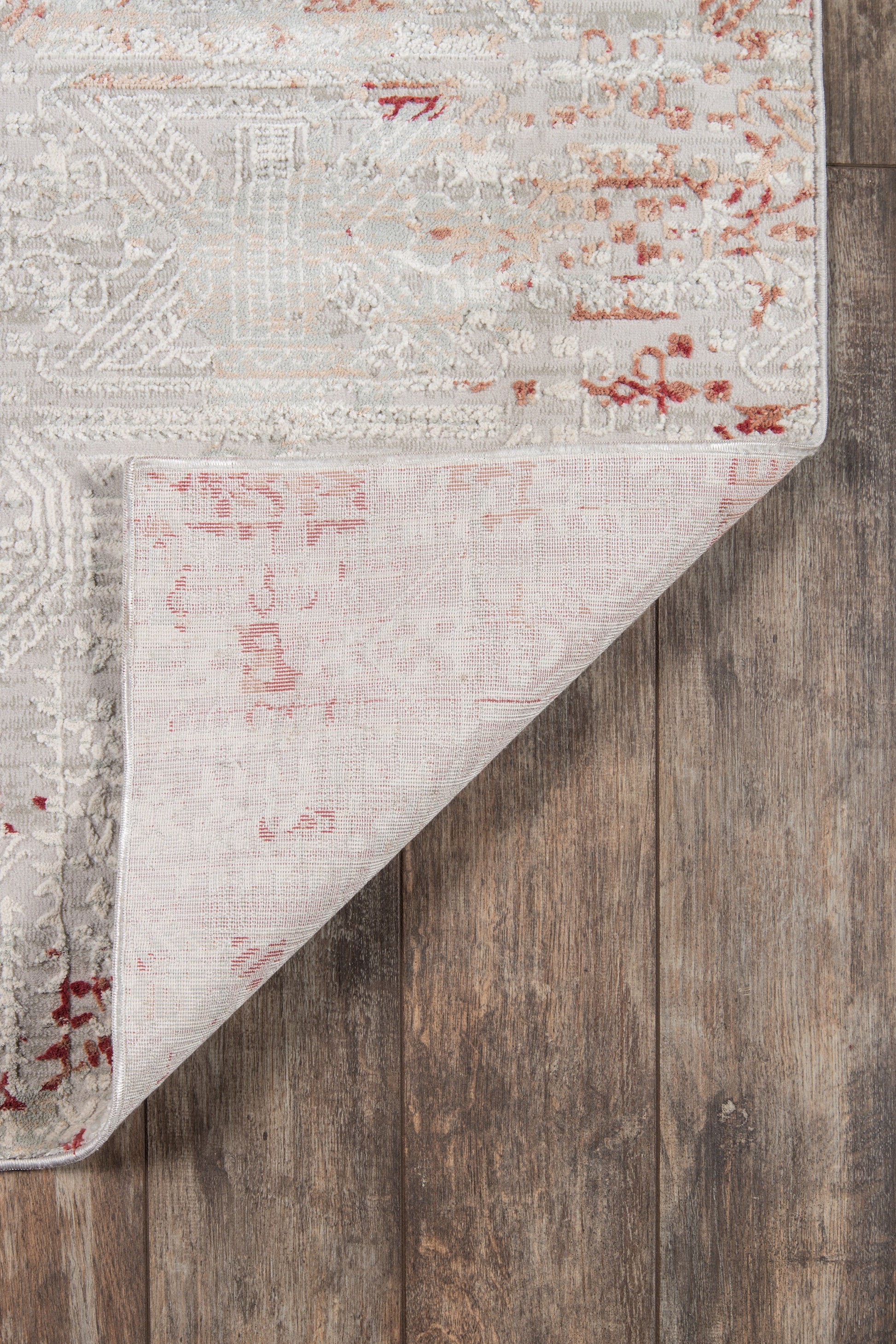 Distressed vintage 2'X8' runner rug in ivory and gray with pink and red accents, folded corner on wooden floor.